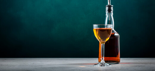 Spanish sherry brandy in glass with bottle on dark green background