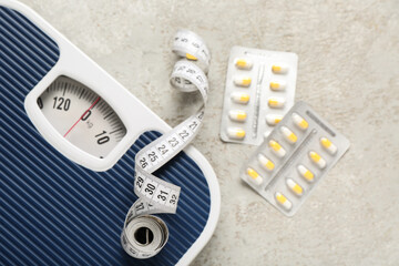 Blister packs with weight loss pills, scales and measuring tape on grey grunge background