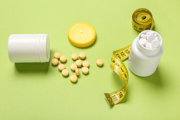 Bottles with weight loss pills and measuring tape on green background