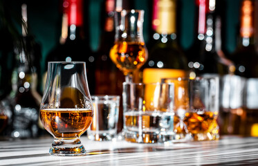 Single malt Scotch whisky in glencairn glass oand bottles of strong drinks n dark green background