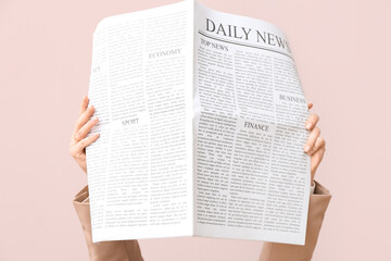 Female hands with daily newspaper on pink background