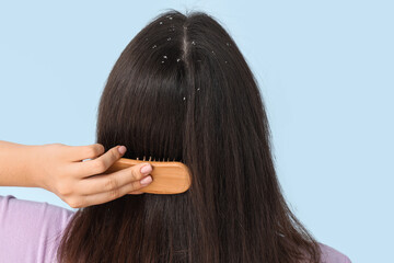 Naklejka premium Young woman with dandruff problem combing hair on blue background, back view