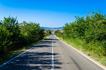 Una strada attraversa la campagna toscana in una giornata estiva di sole e cielo terso