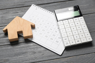 Wooden house figure, calendar and calculator on grey wooden background. Debt concept