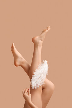 Legs of young woman with soft feather on brown background. Epilation concept