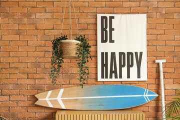 Surfboard, paddle and wooden chest of drawers near brick wall