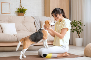 Young sporty woman with cute Beagle dog on yoga mat in living room