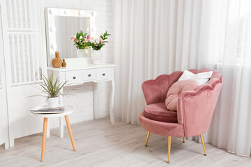 Interior of living room with pink armchair, chest of drawers, houseplant and coffee table