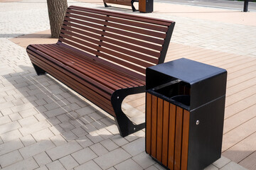 A modern urban bench with metal frame and wooden slats, placed on a paved public square next to a...