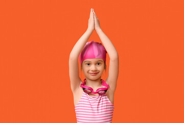 Cute little girl in swimsuit with swimming hat and goggles on orange background