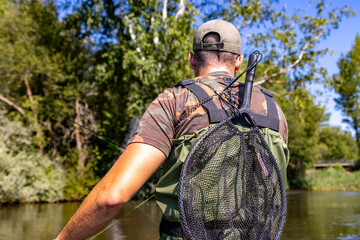 Back view of man fly fishing with net in outdoor setting