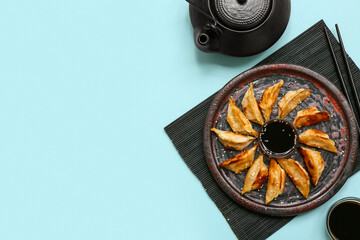 Plate of fried Japanese gyoza with bowls of soy sauce and teapot on blue background