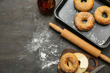 Wooden board and baking dish of tasty bagels with sesame seeds on black background