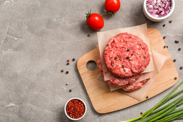 Cutting board with raw meat cutlets on grey grunge background