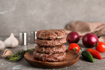 Wooden plate with stack of tasty meat cutlets, vegetables and spices on grey grunge background