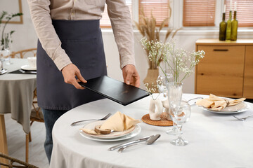 Male waiter putting menu on table in restaurant