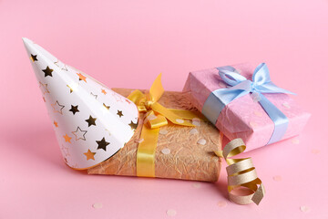 Party hat with gift boxes and confetti on pink background