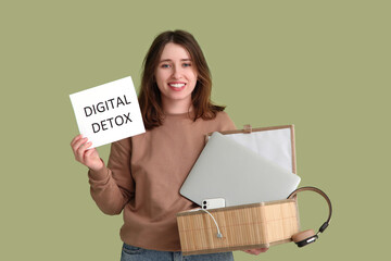 Young woman holding paper with text DIGITAL DETOX and gadgets in box on green background. National...