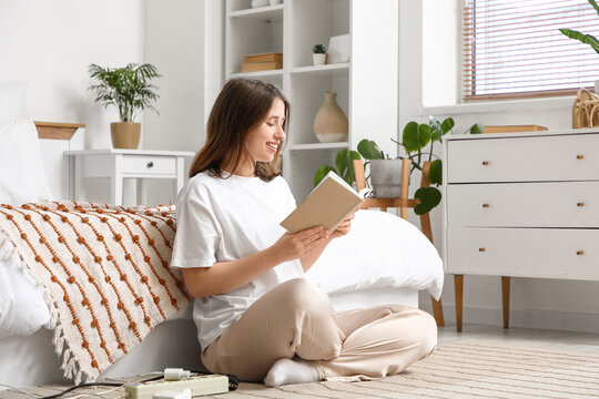 Young woman with plugs reading book in bedroom. National Day of Unplugging