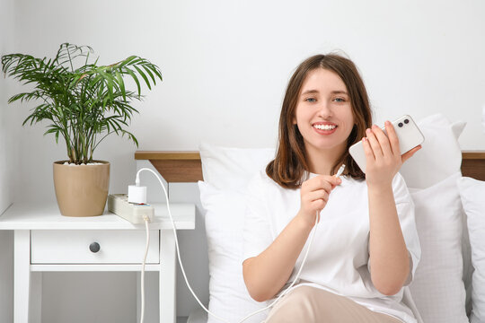 Young woman getting out charger from mobile phone in bedroom. National Day of Unplugging