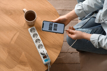 Young woman getting out charger from mobile phone with text DIGITAL DETOX at home, top view....