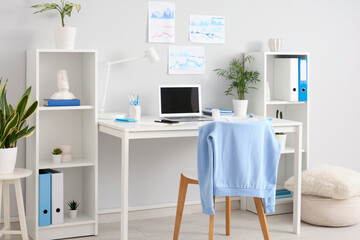 Interior of light office with workplace, shelf units and plants