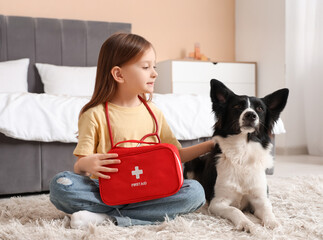 Cute little girl with first aid kit and dog on carpet in bedroom