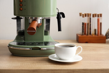 Coffee machine and cup of espresso on table in kitchen, closeup