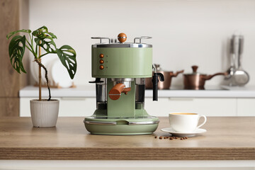 Coffee machine with cup of espresso and plant on table in kitchen