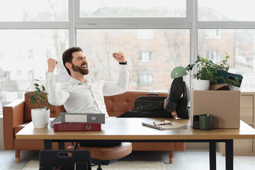 Happy fired young man sitting at table in office