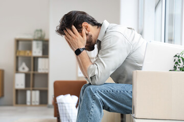 Upset fired young man sitting on windowsill in office