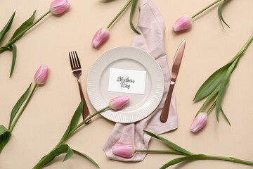 Beautiful table setting with greeting card and tulip flowers on beige background. Mother's Day celebration