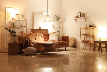 Interior of living room with brown sofa, shelf units and glowing lamps in evening