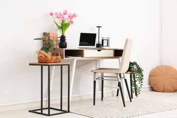 Interior of modern workplace with stools, houseplants, laptop and beautiful tulip flowers in vase