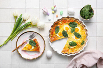 Cut Easter egg tart with spinach leaves and tulip flowers on white tile background