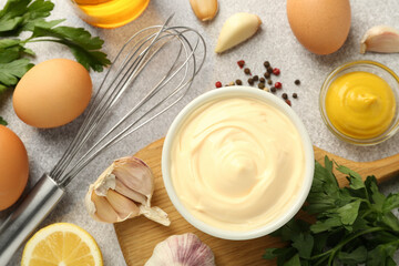 Delicious mayonnaise sauce in bowl, whisk and ingredients on grey table, flat lay
