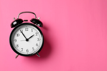 Black alarm clock on pink background, top view. Space for text