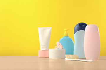 Baby cosmetic products and bath accessories on wooden table against yellow background. Space for text