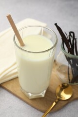 Delicious vanilla milk in glass, pods and spoon on grey table, closeup