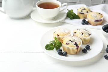 Delicious muffins with blueberries, powdered sugar and mint on white wooden table. Space for text