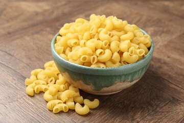 Raw horns pasta in bowl on wooden table, closeup