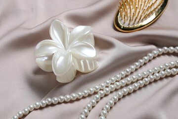Beautiful hair clip, pearl necklace and brush on beige fabric, closeup