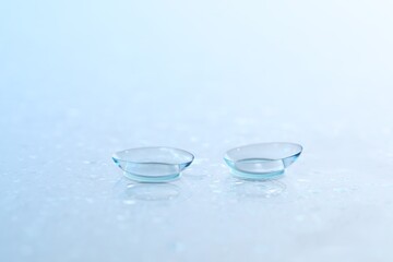 Pair of contact lenses and water drops on light mirror surface, closeup