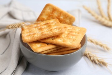 Tasty salty crackers with wheat spikes on white table, closeup