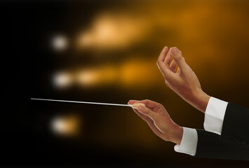Conductor directing orchestra with baton in concert hall, closeup