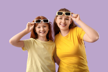 Beautiful young woman with her cute daughter in stylish sunglasses on lilac background. Mother's...