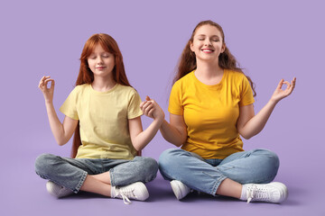 Beautiful young woman with her cute daughter meditating on lilac background. Mother's Day...