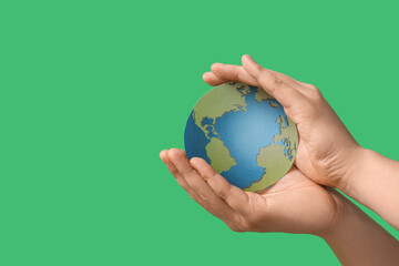 Female hands with paper Earth on green background. Ecology concept