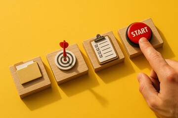 Finger pressing red start button next to checklist, target and folder icons on wooden blocks over yellow background, symbolizing beginning of planning