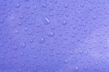 Water drops on purple plastic as a background macro photo.